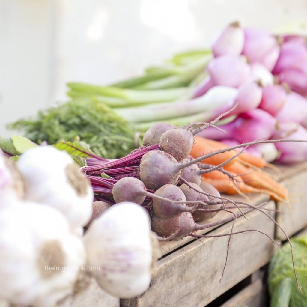 Fresh beets, radishes, carrots, and garlic displayed at a farmers market stand